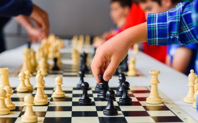 Child's hand moves the horse during a chess tournament with several game boards.